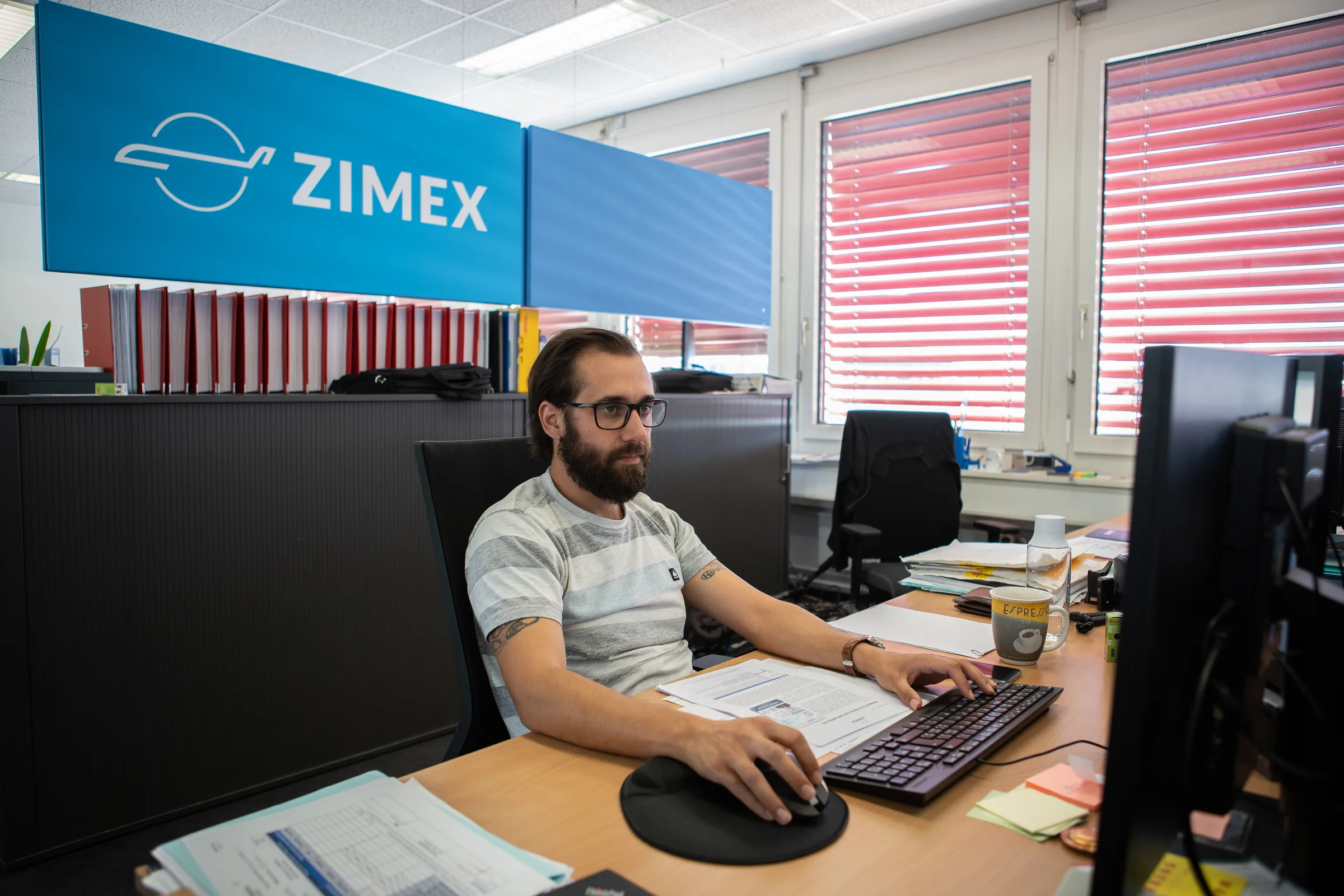 A Zimex colleague at his desk in the Glattbrugg office under the Zimex sign.