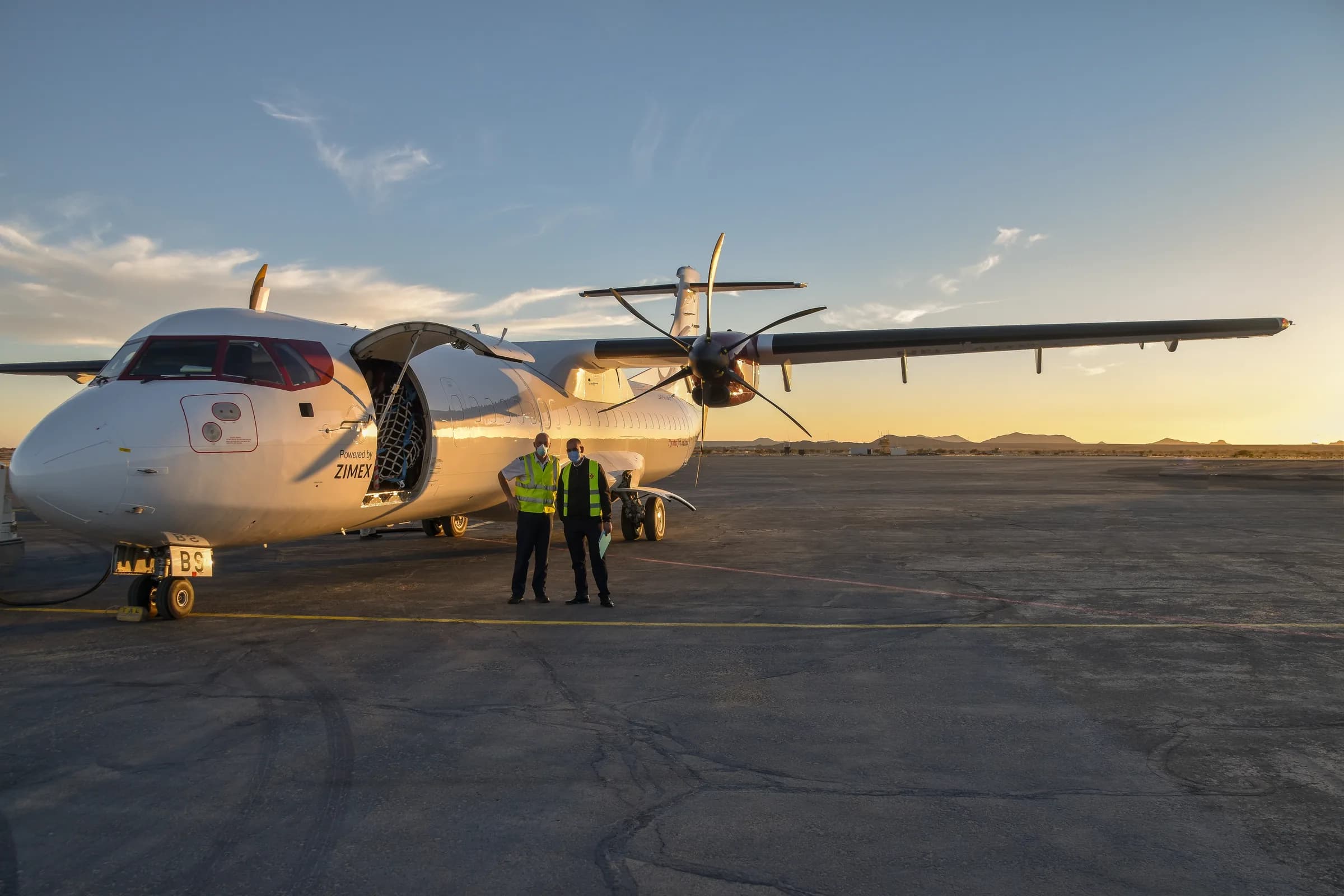 Zimex crew in front of an ATR 72 freighter with its cargo door open at dusk