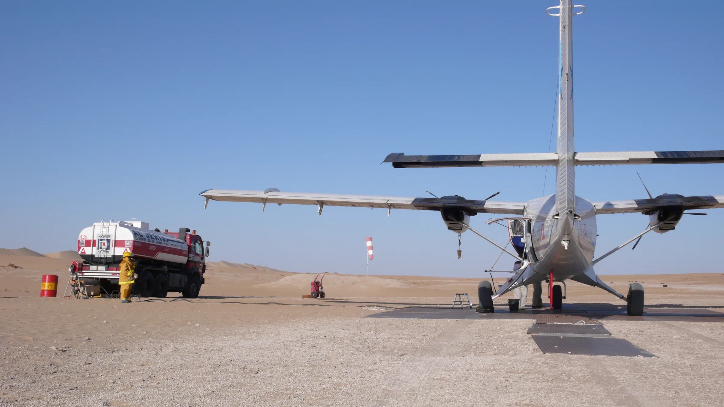 A Twin Otter being refuelled from a tanker truck on a gravel desert strip