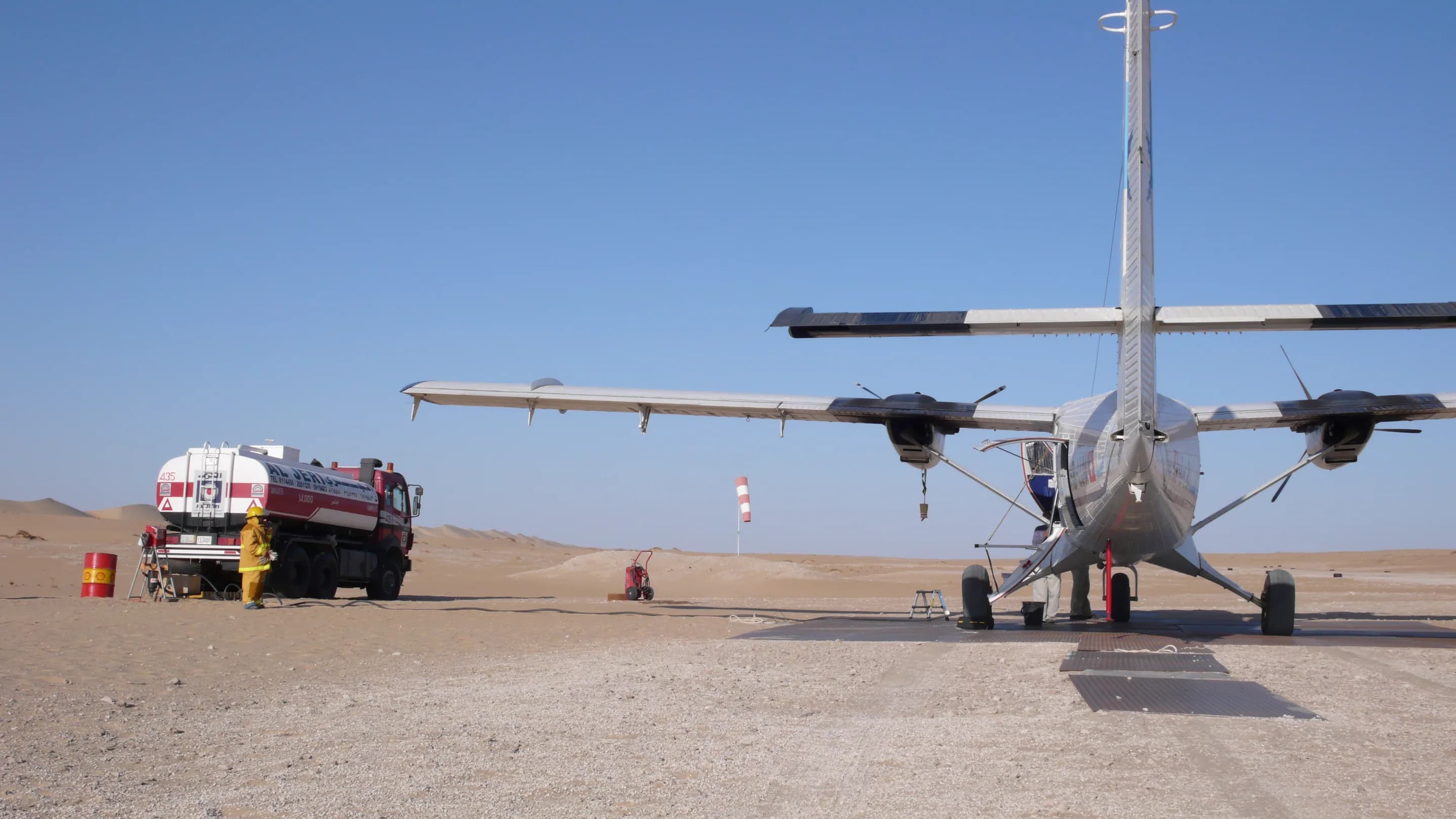 A Twin Otter seen from behind on a desert strip, a fuel truck alongside