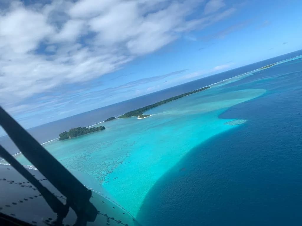 A turquoise lagoon and reef seen past the wing strut of a Twin Otter