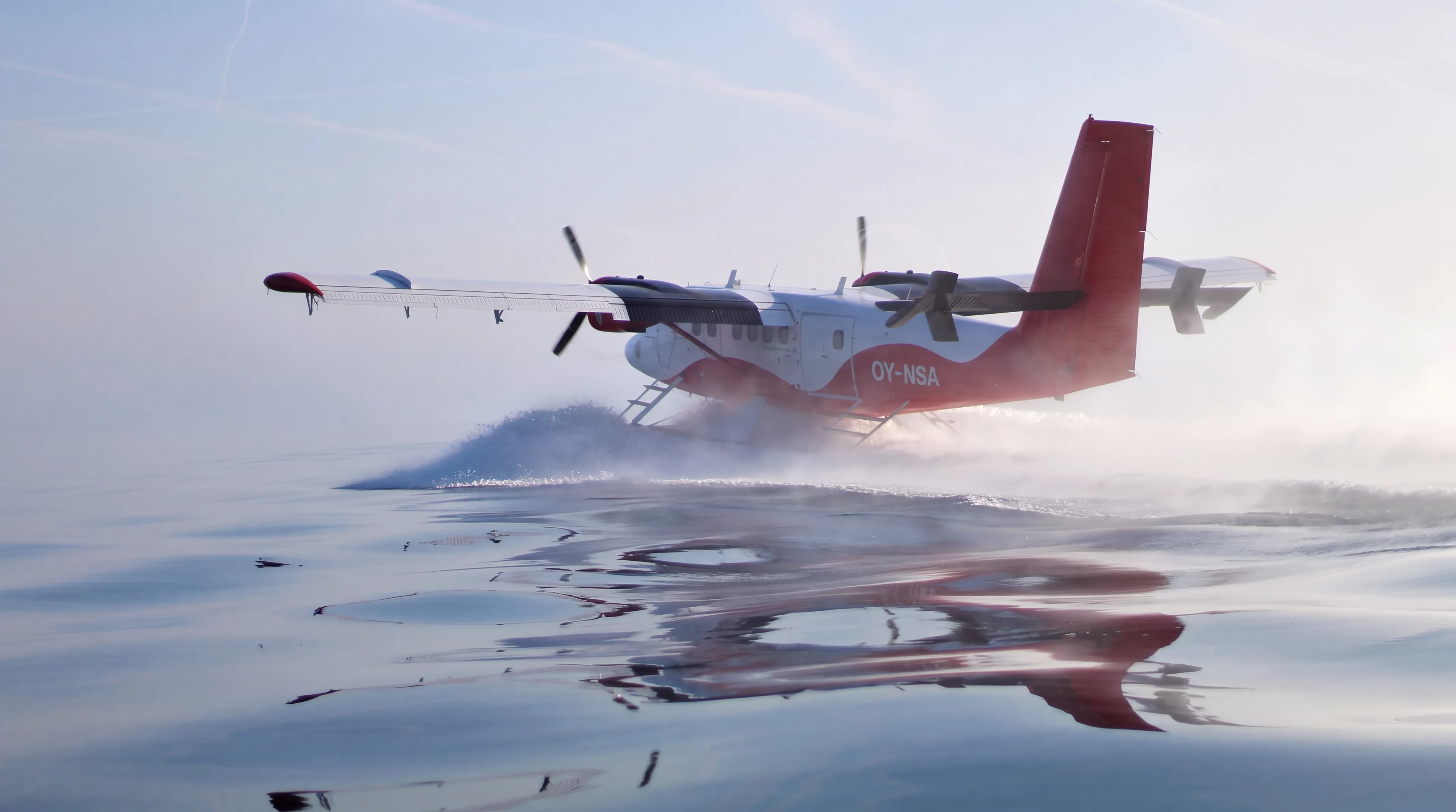 Red and white Twin Otter on floats taking off from calm water